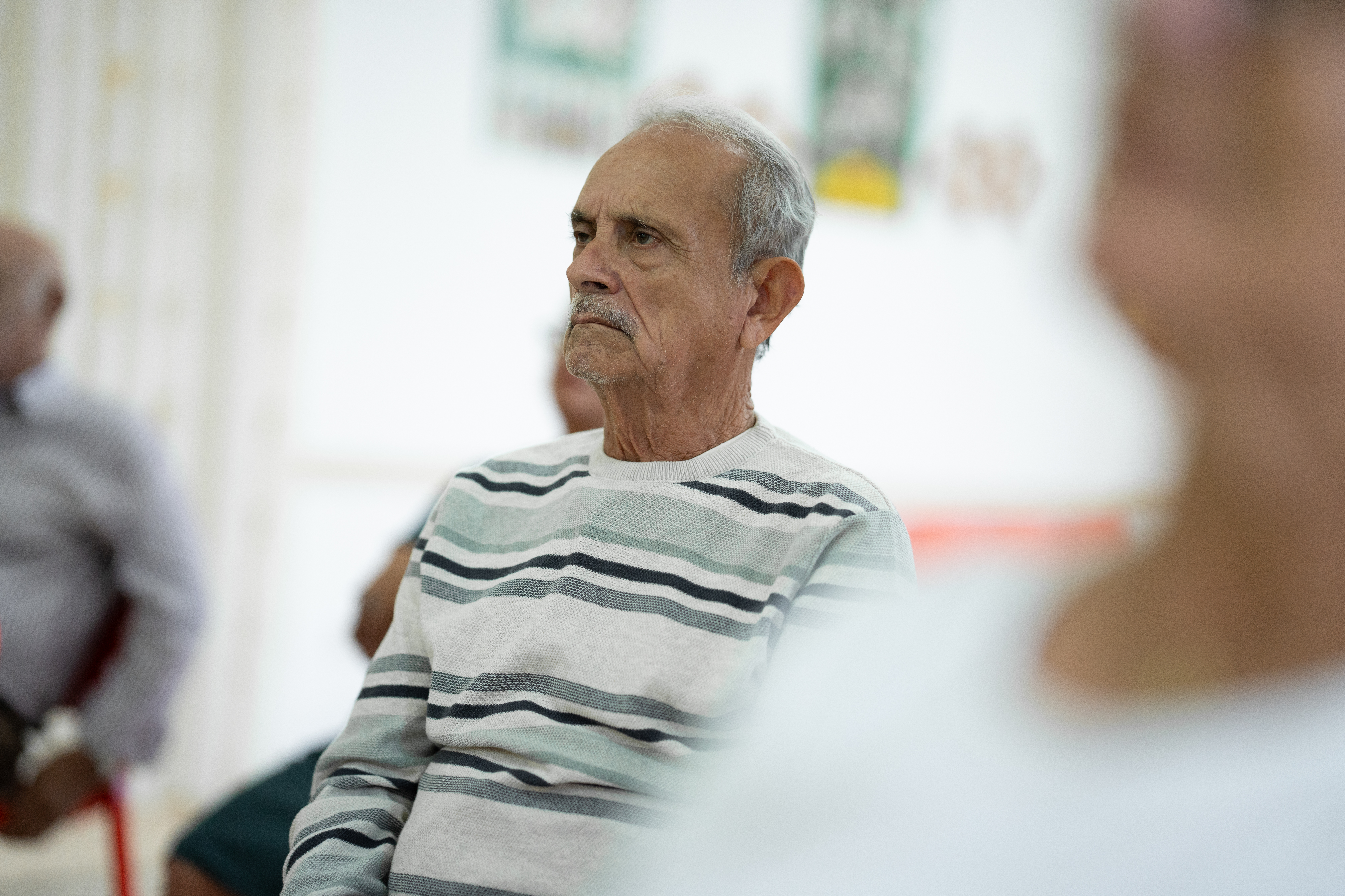 Hombre mayor escuchando atentamente en actividad grupal en interior con fondo desenfocado