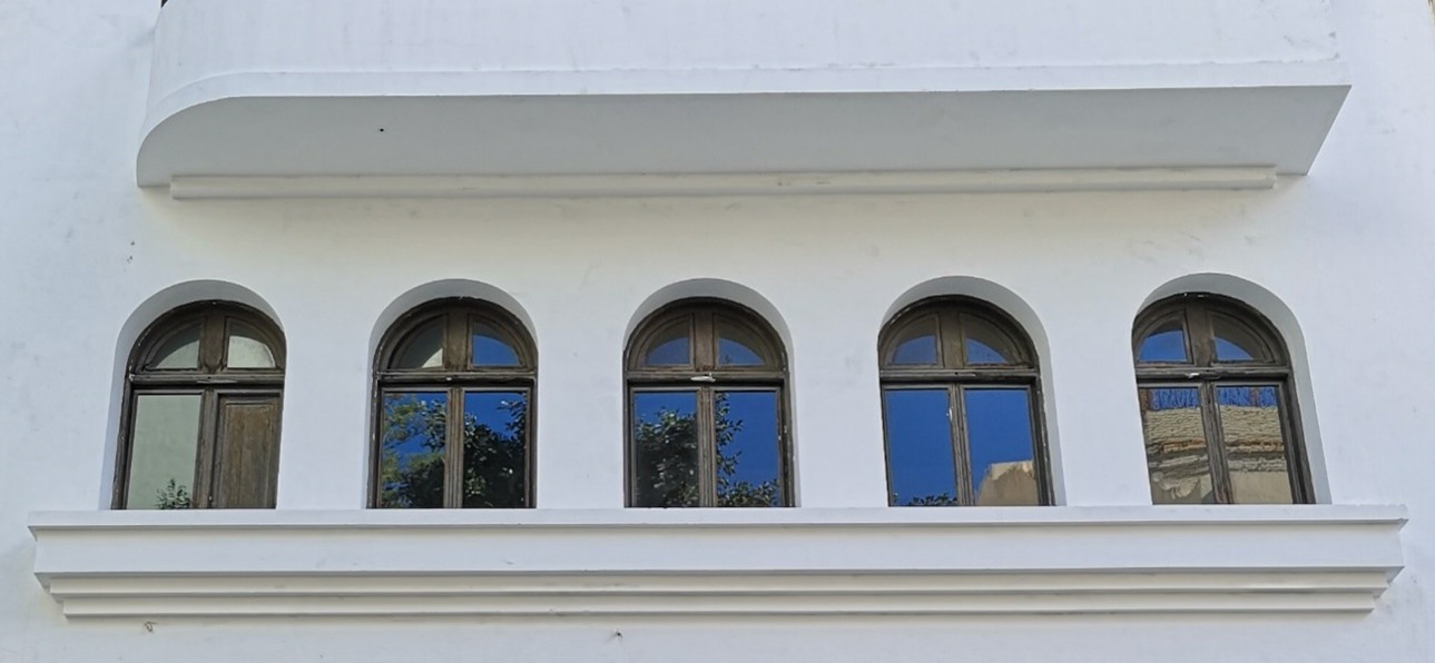 Detalle de fachada blanca con ventanas arqueadas alineadas y reflejos en los cristales en edificio urbano